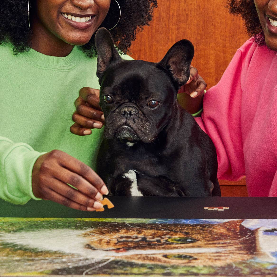 Two women with a black dog playing with a puzzle