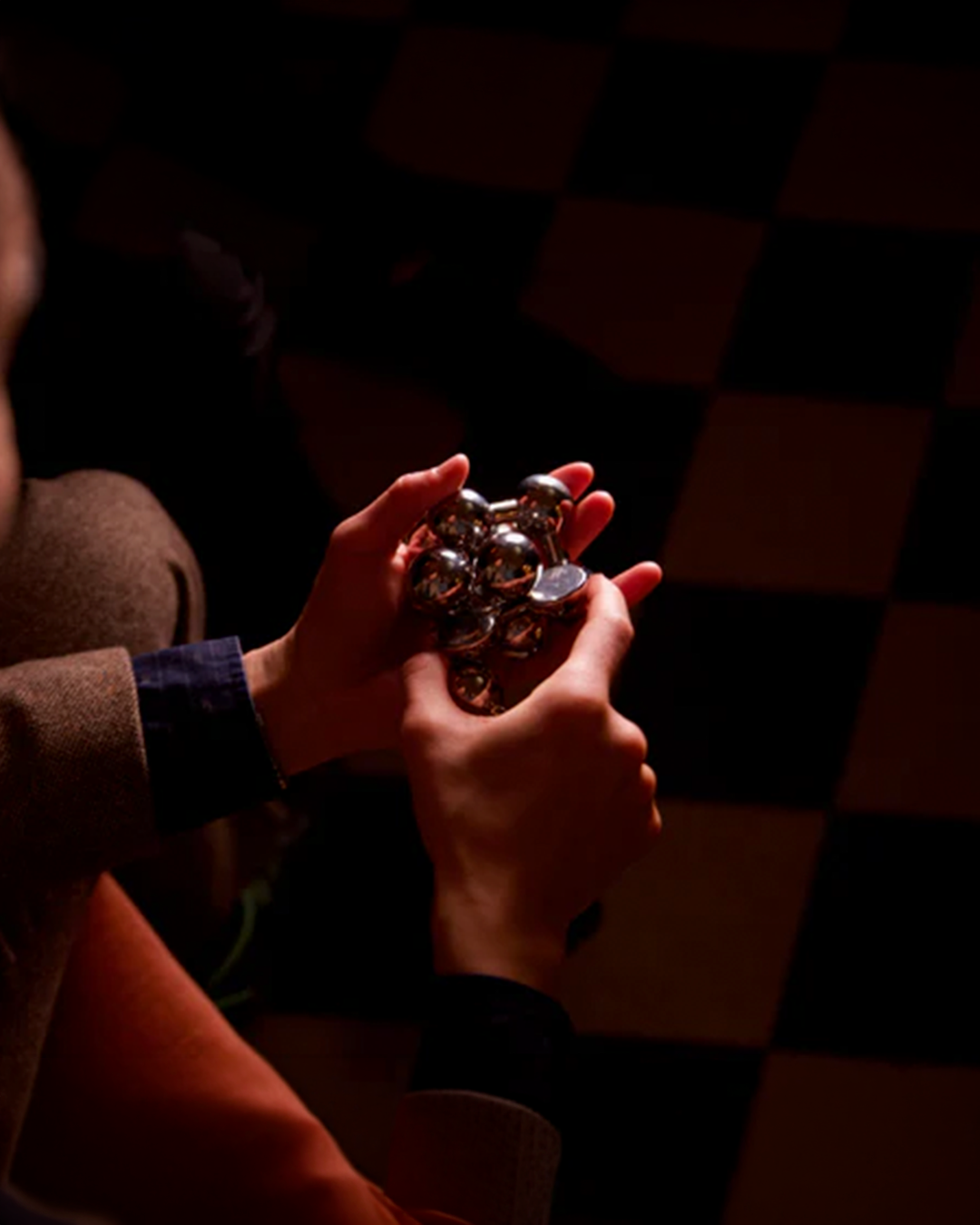 Person holding a metallic object against a dark checkered background
