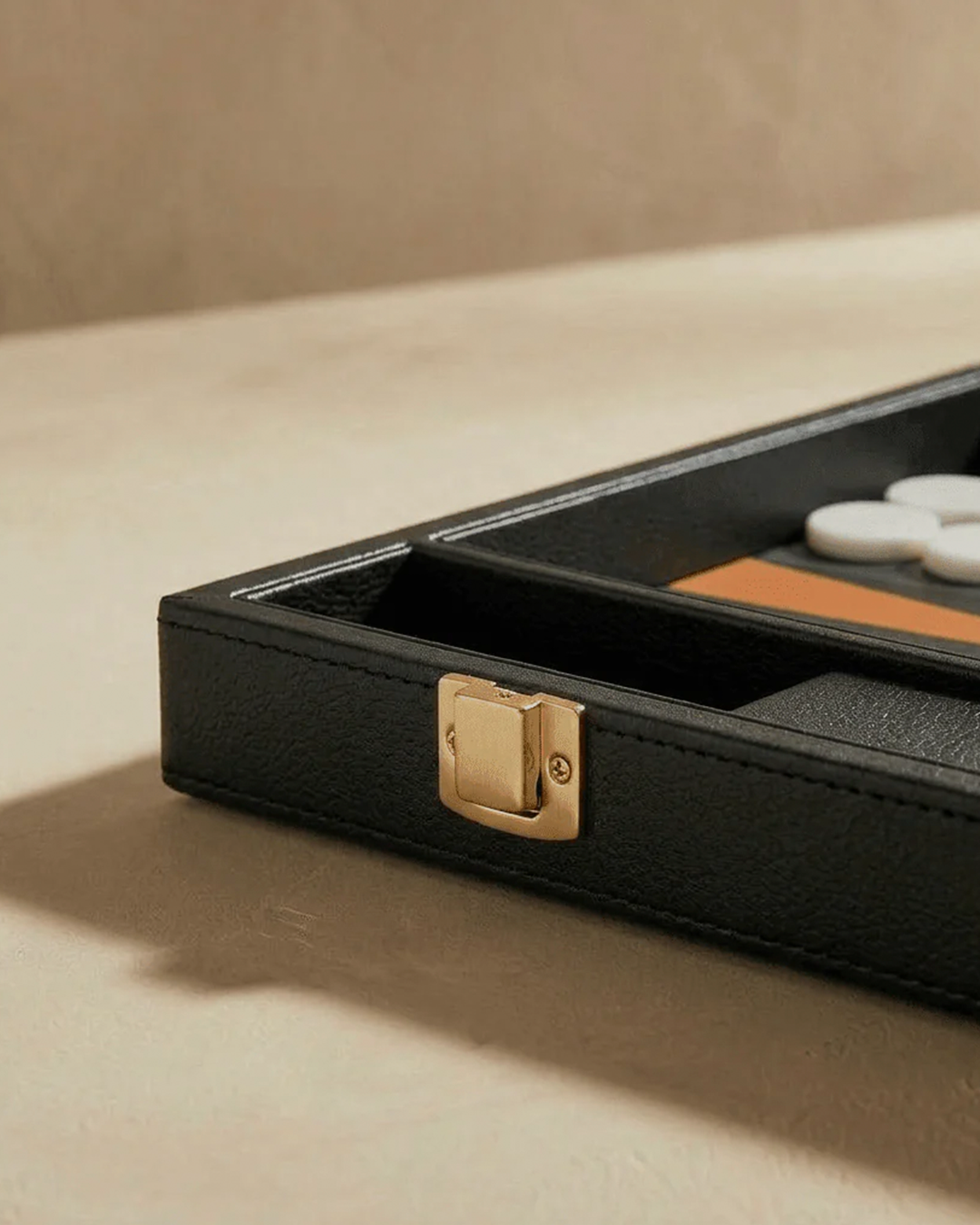Black leather case with gold clasp on a beige surface