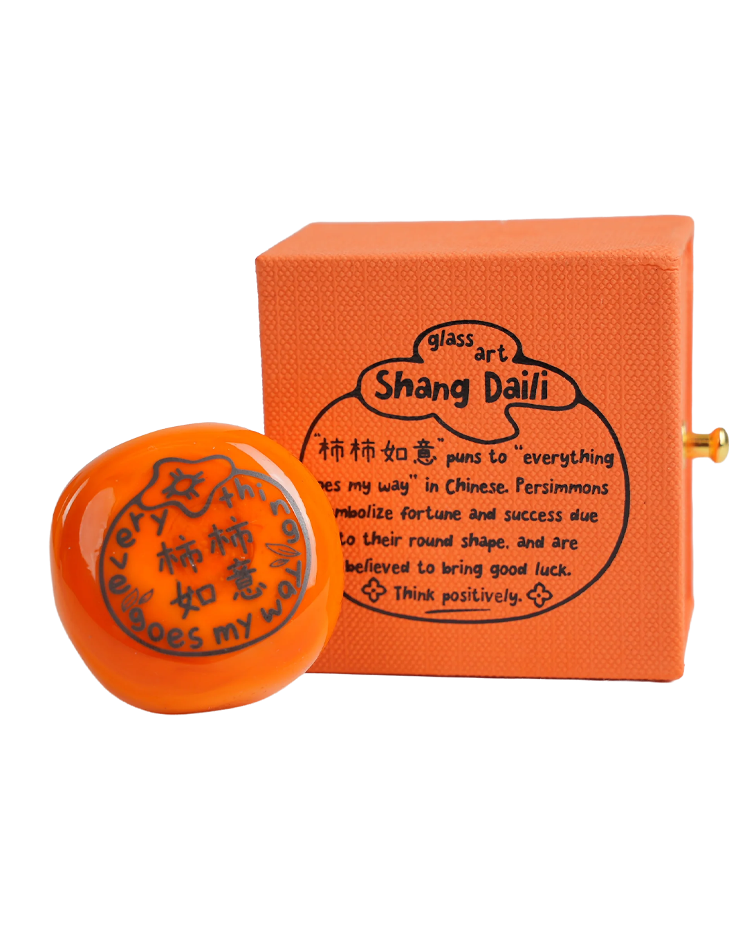 A persimmon glass art figurine and its matching textured orange box with black printed text, set against a plain white background.