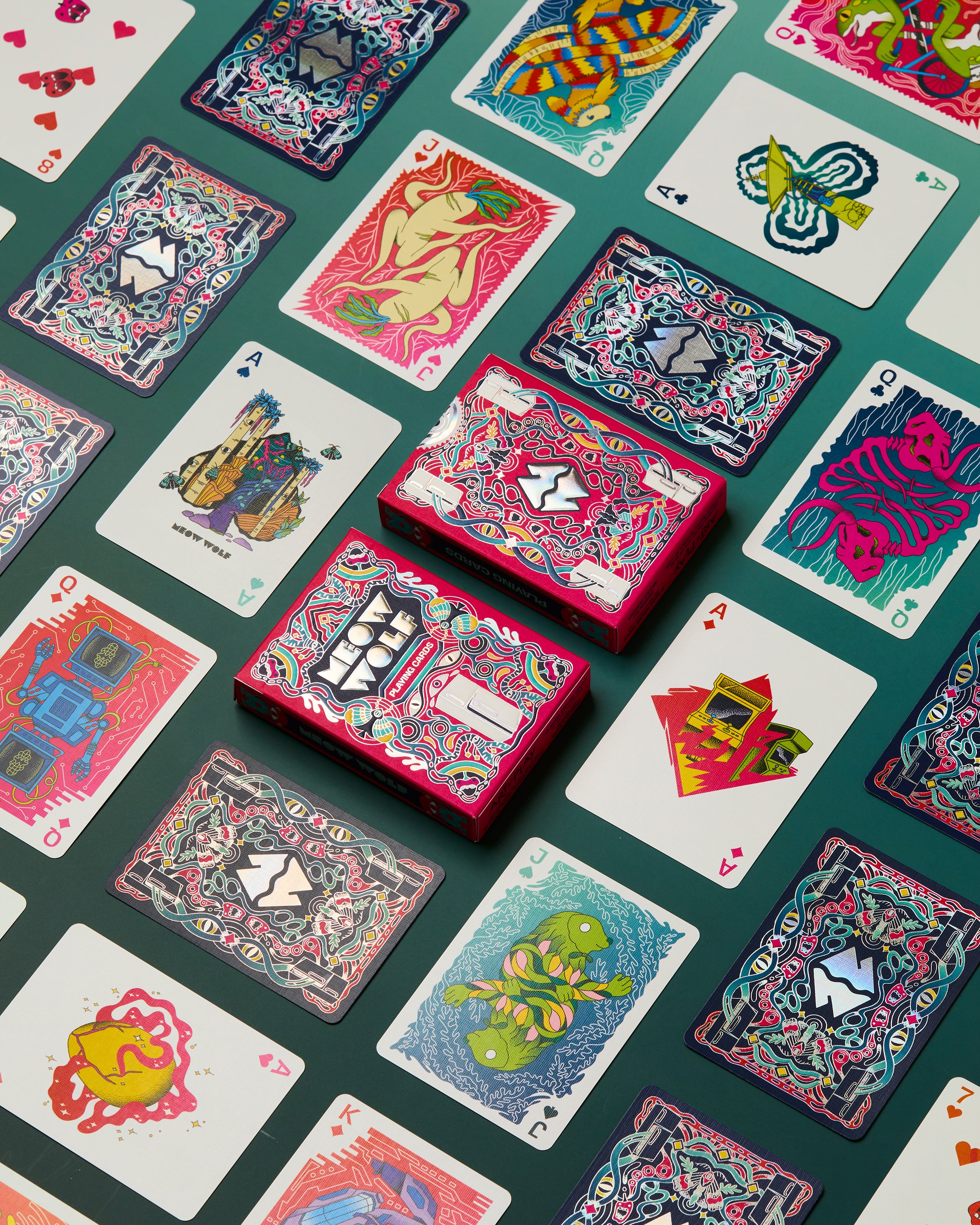 A styled flat-lay of a deck of playing cards on a dark green background, with several cards face-up and the deck box stacked in the center. The artwork is highly detailed, colorful, and psychedelic, featuring various abstract and illustrative designs in pink, blue, yellow, and green.