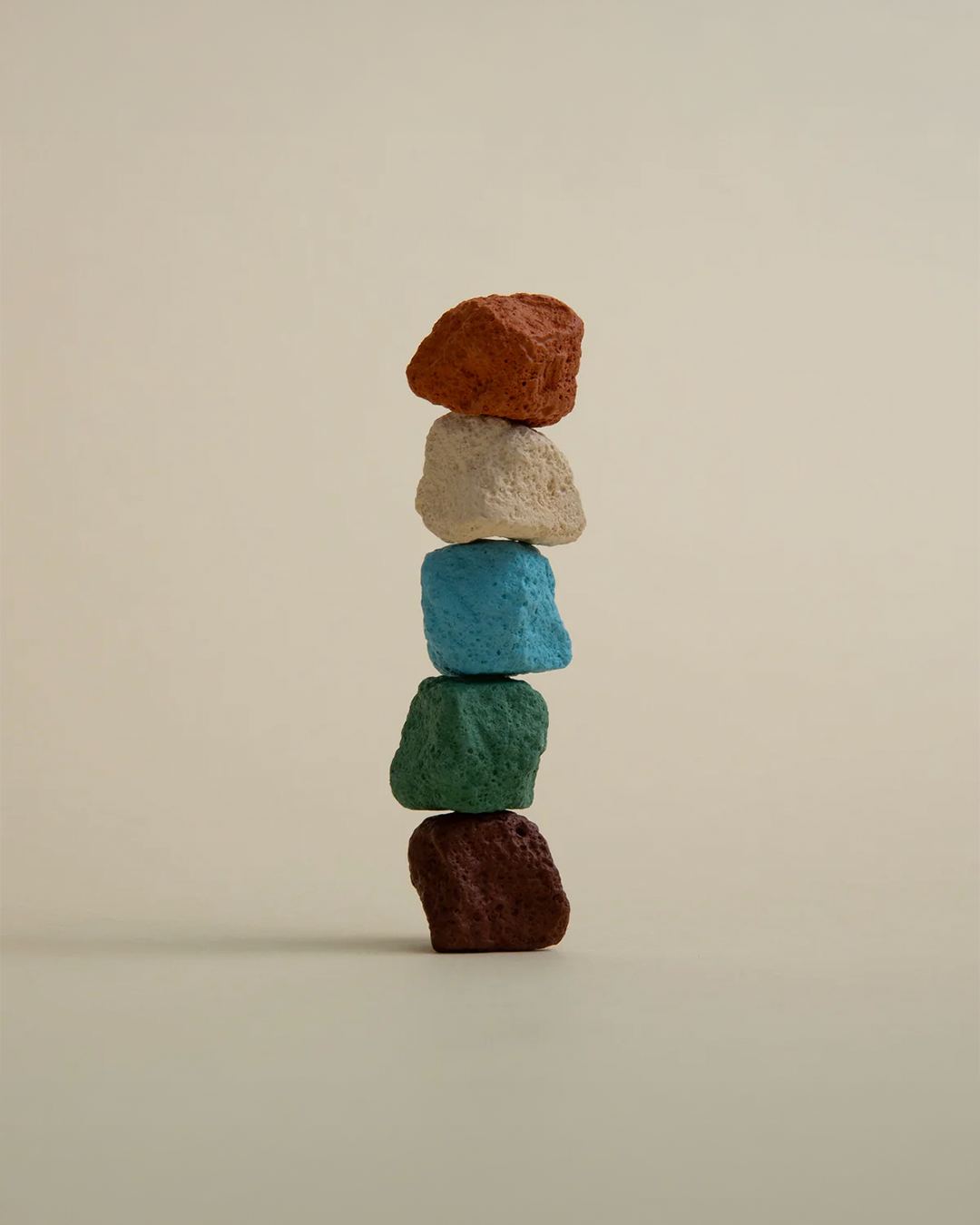 A stack of five textured, rough-colored stones balanced vertically on a plain, warm beige background.
