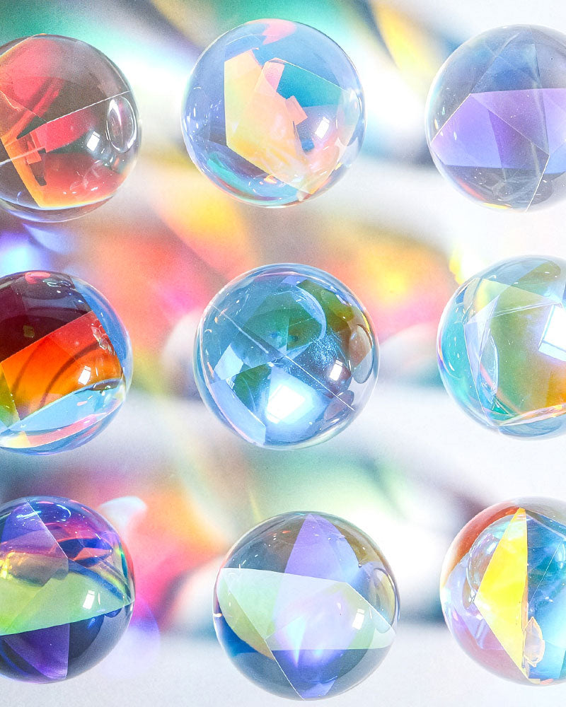Nine iridescent glass marbles arranged in a grid, each reflecting and refracting rainbow colors against a soft, blurred multicolor background.