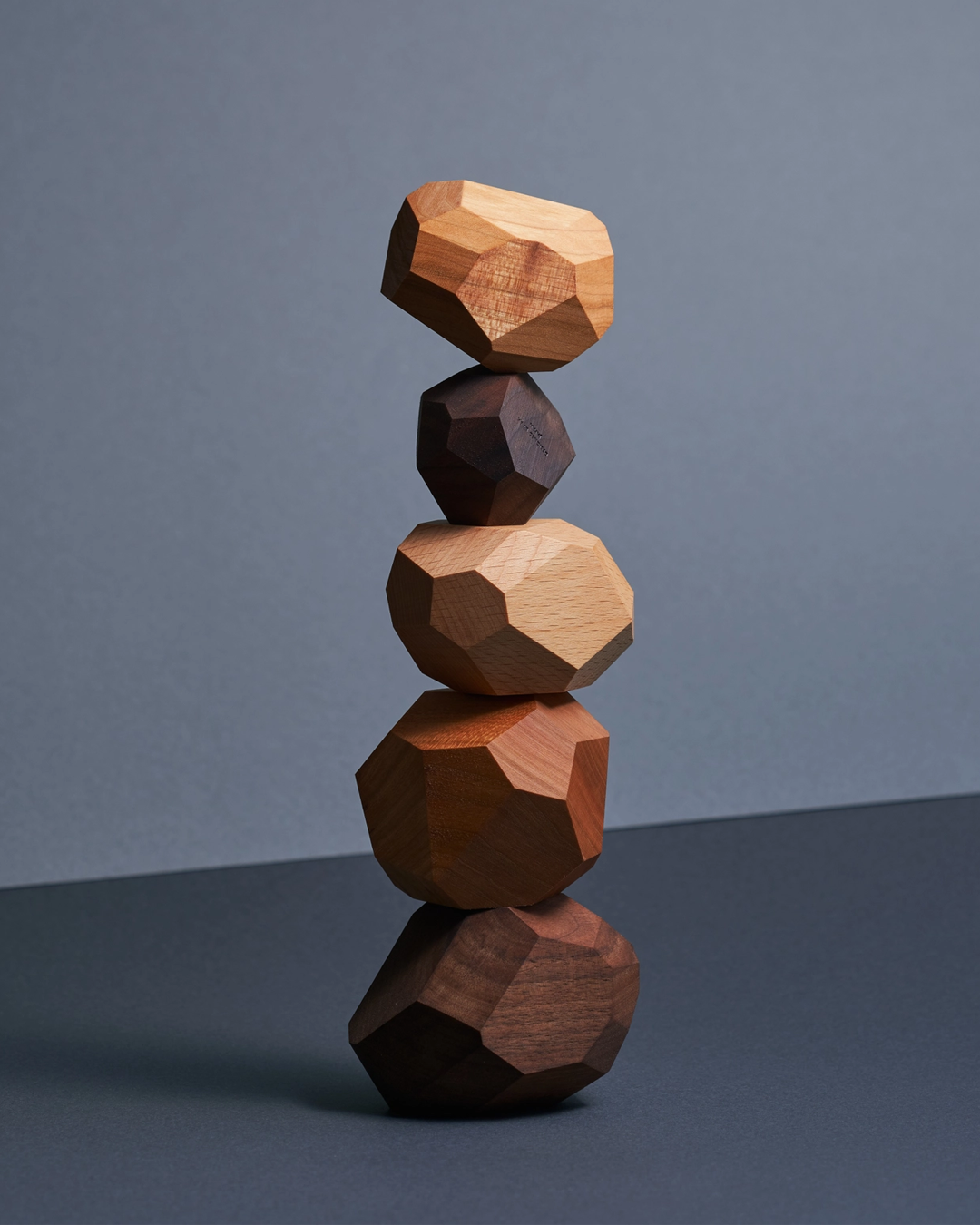 Stack of geometric wooden blocks on a reflective surface with a gray background