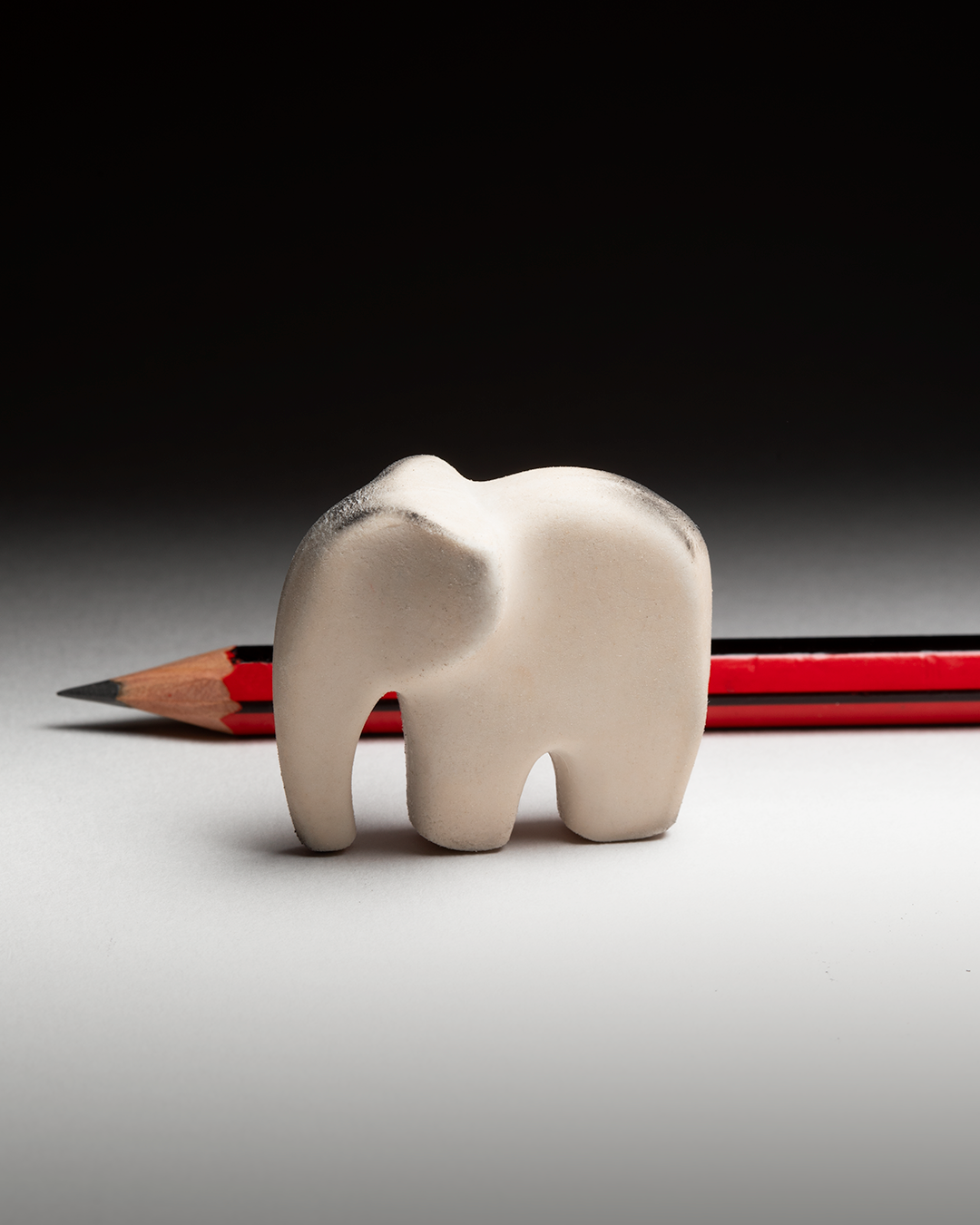 A small white eraser in the form of elephant with a red pencil in the background.