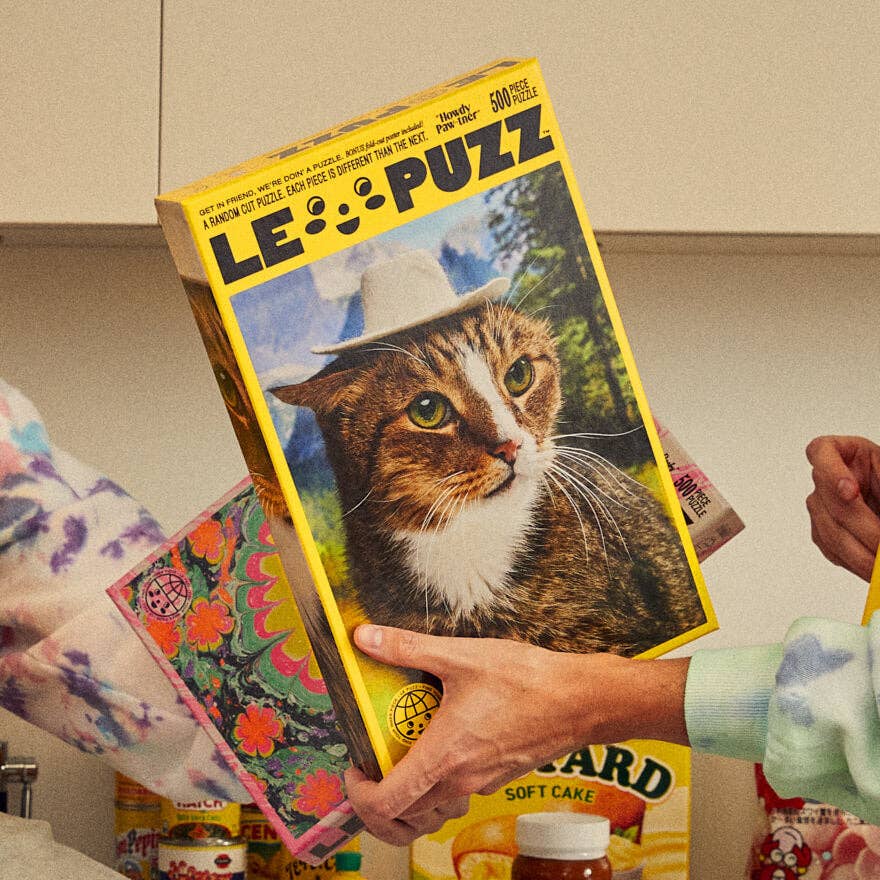 Person holding a Le Puzz puzzle box with a cat illustration on a neutral background