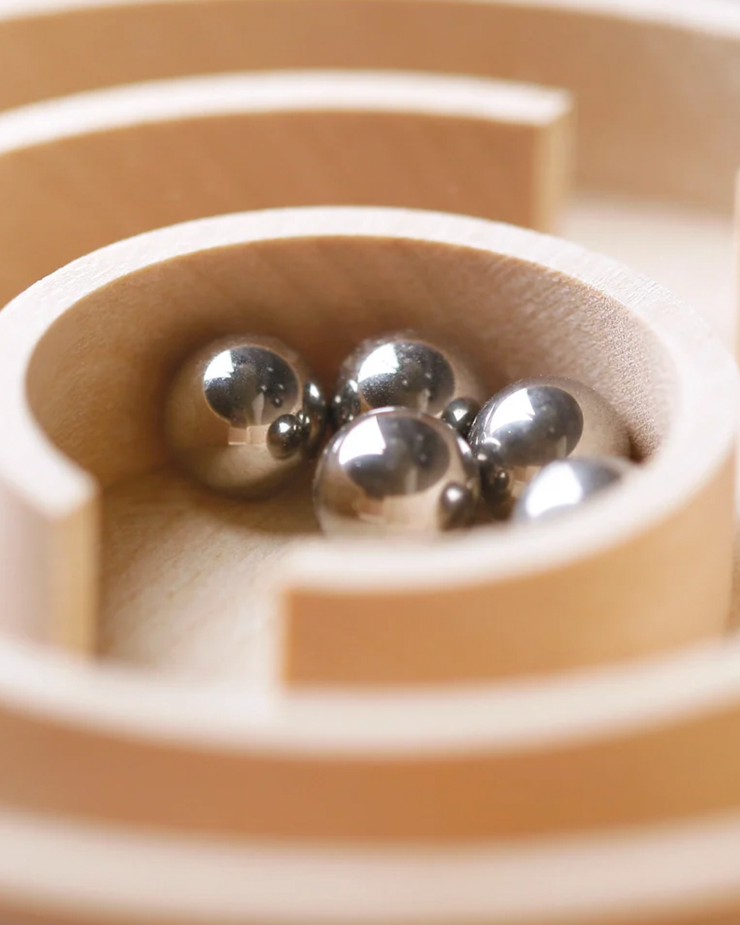 Close-up of several reflective silver metal balls resting inside a shallow wooden bowl or tray.