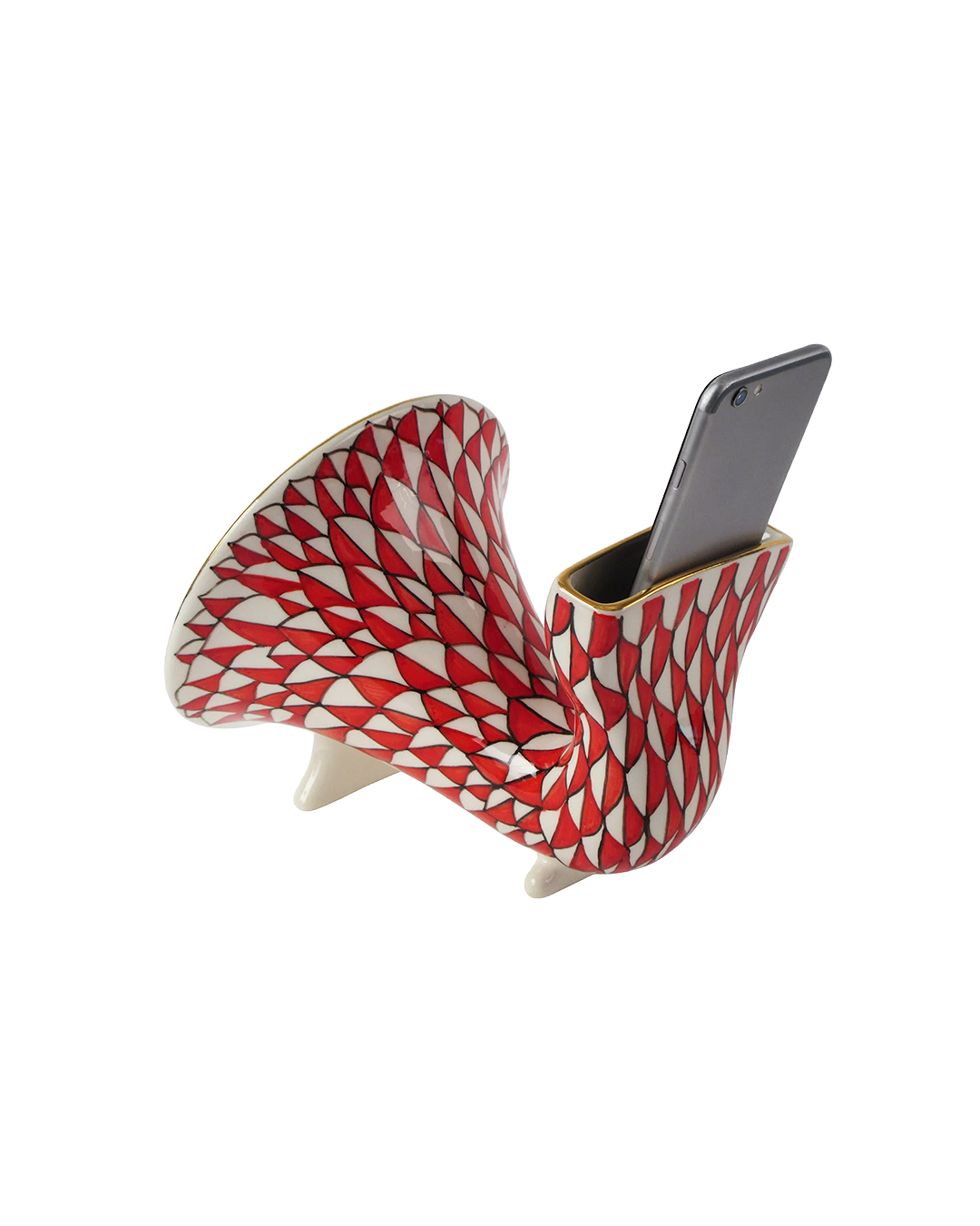 A sculptural ceramic phone stand with a red and white geometric pattern, holding a black smartphone, set against a plain white background.