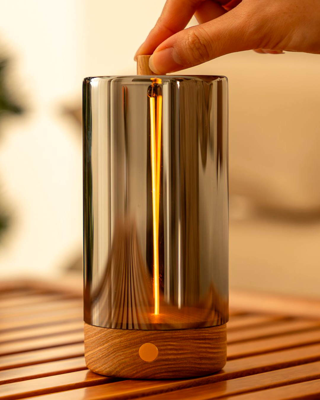 Hand holding a wooden and glass diffuser on a wooden surface with a blurred background