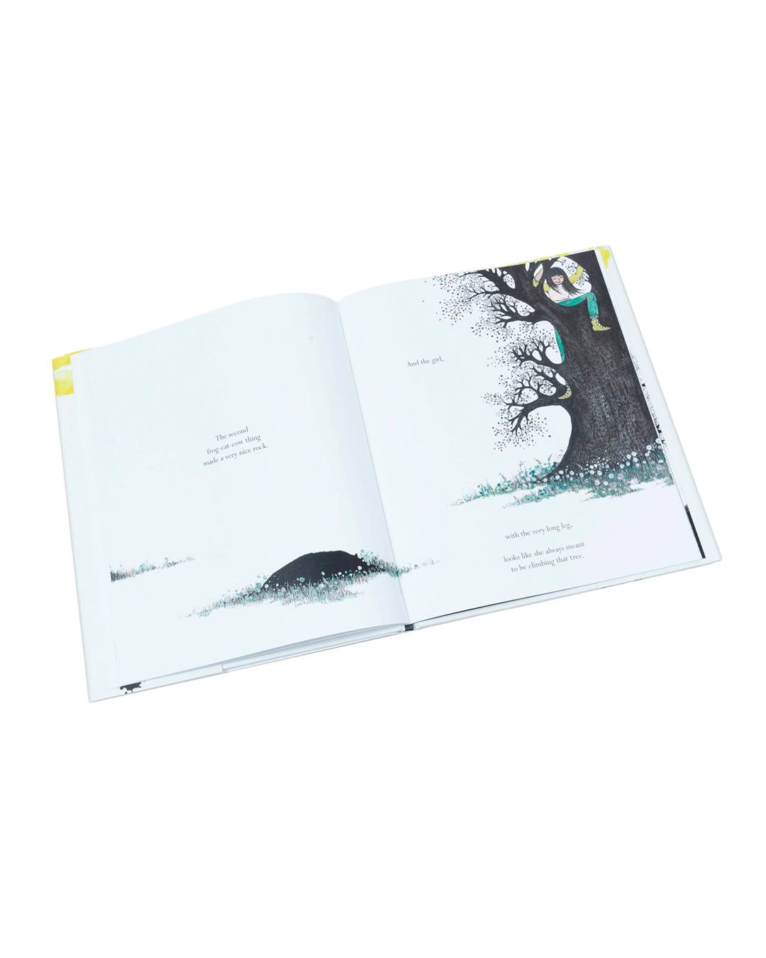 An open children's book with illustrated pages, photographed on a clean white background. The right page shows a large black tree with blue-gray ground and small colorful bird silhouettes, while the left page has a simple dark shape and text.