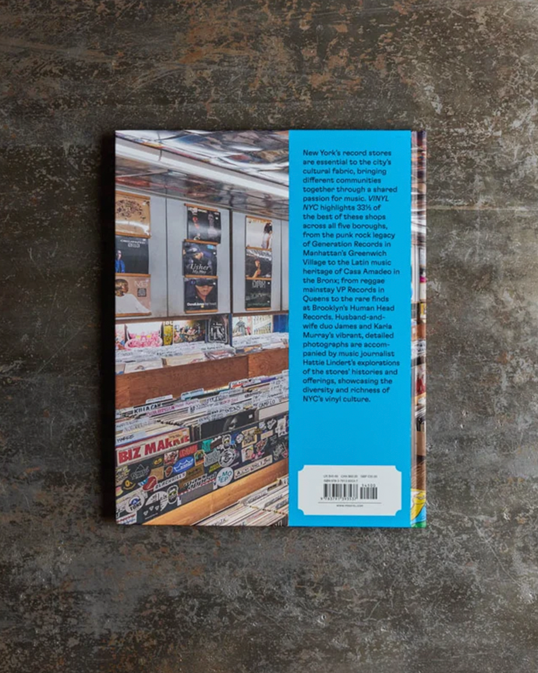 A book or magazine lying flat on a textured dark gray surface, showing the back cover with a large blue vertical band and a photo of a record store interior on the left side.