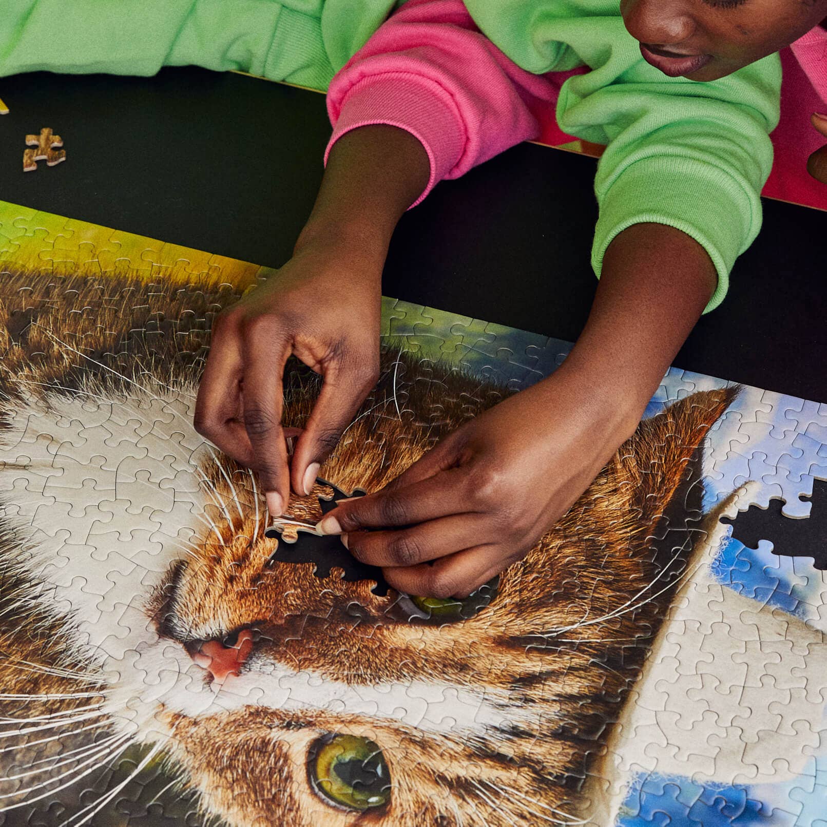 Person assembling a puzzle of a cat's face with a green shirt and pink sleeves.