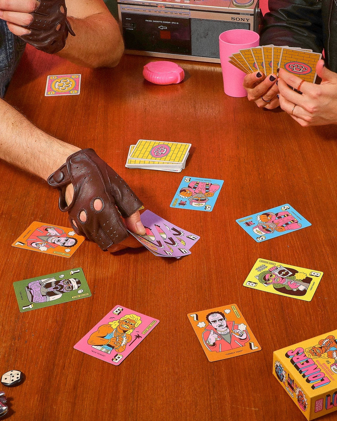 Two people playing a card game with colorful cards on a wooden table.