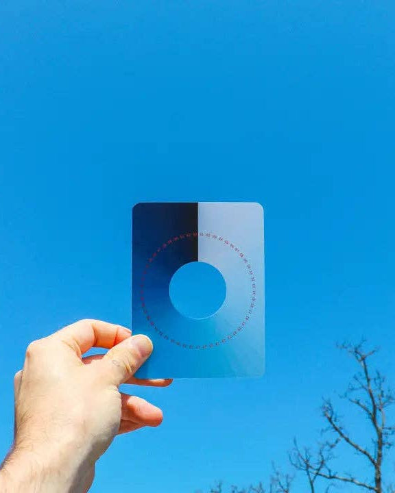 Hand holding a square filter with color swatches against a clear blue sky