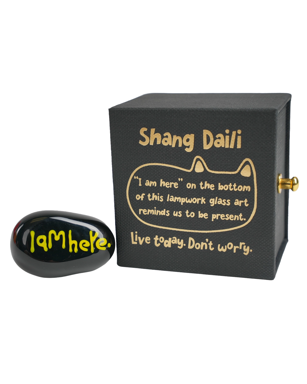A black square lampwork glass art box with gold lettering and a gold winding key, shown next to a matching black oval glass art piece with yellow 'I AM HERE.' text.