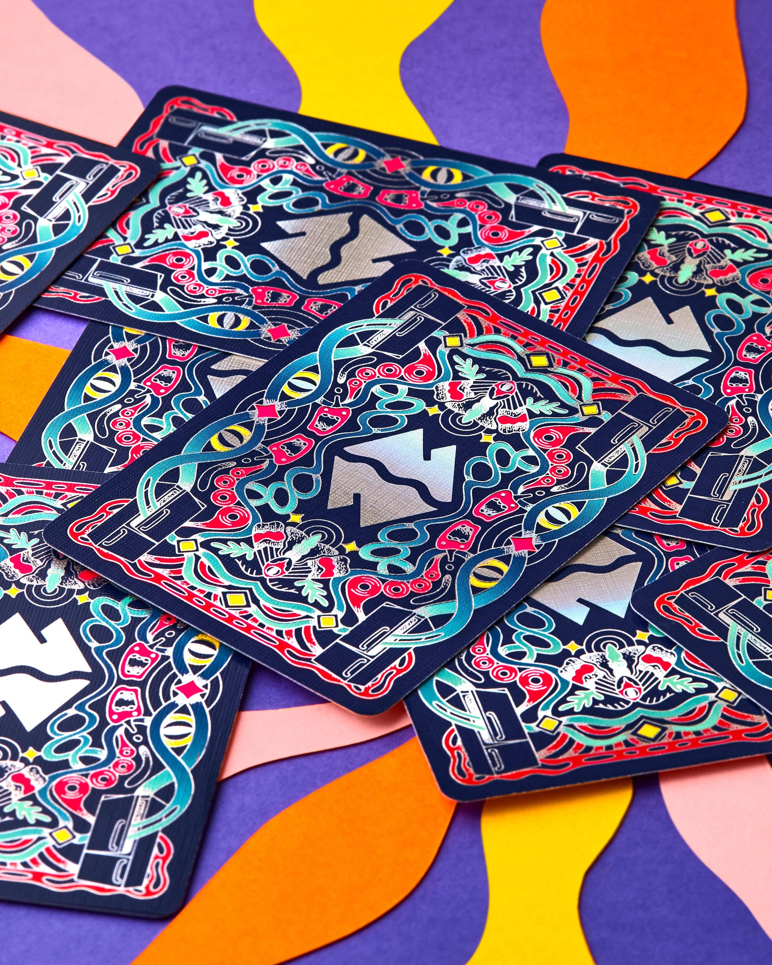 A close-up of several overlapping playing cards with an intricate psychedelic illustration featuring snakes, eyes, and abstract shapes in red, teal, yellow, pink, and black, set against a colorful wavy background.