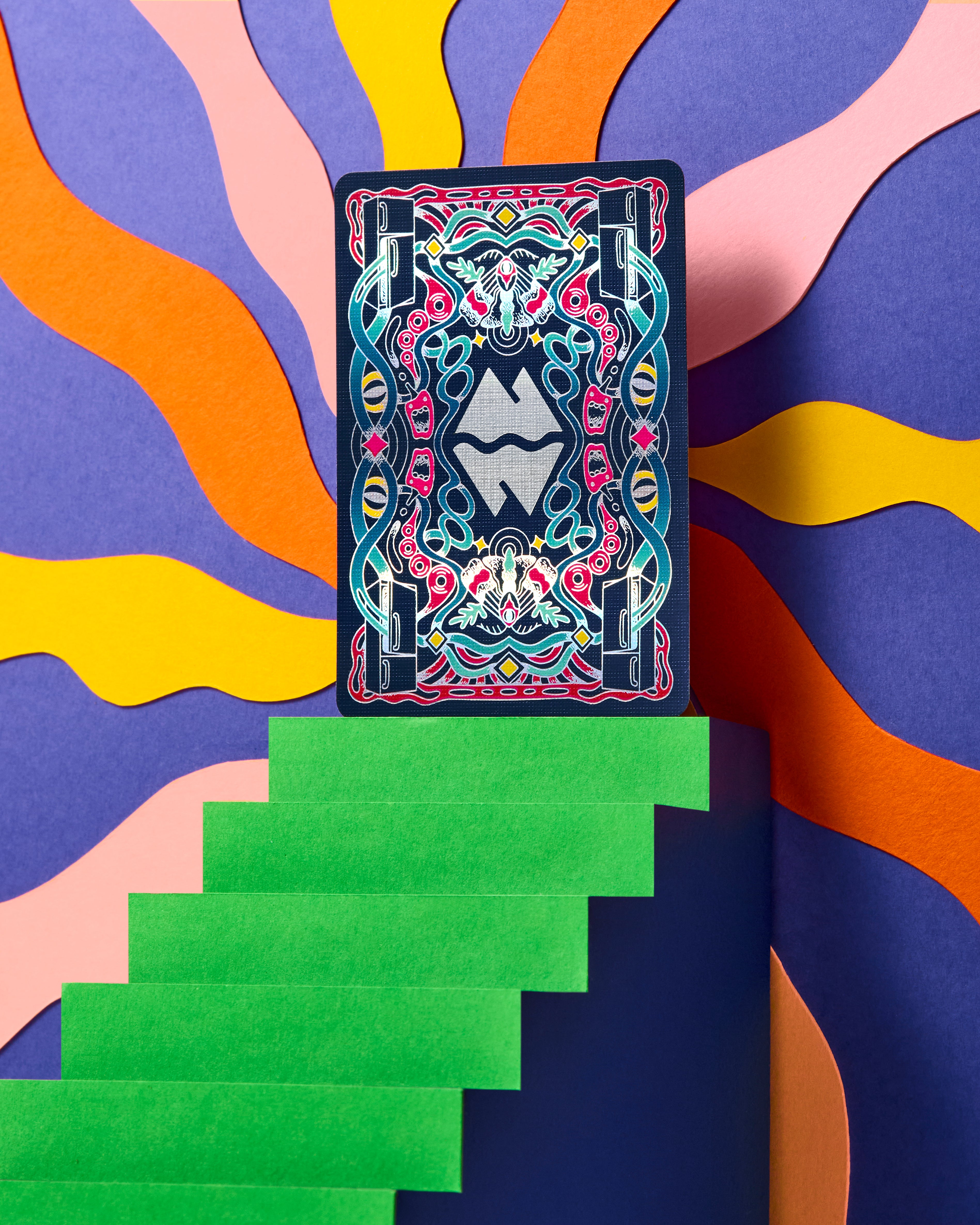 A single illustrated playing card stands upright on green steps against a colorful abstract background with wavy orange, yellow, pink, and purple shapes.