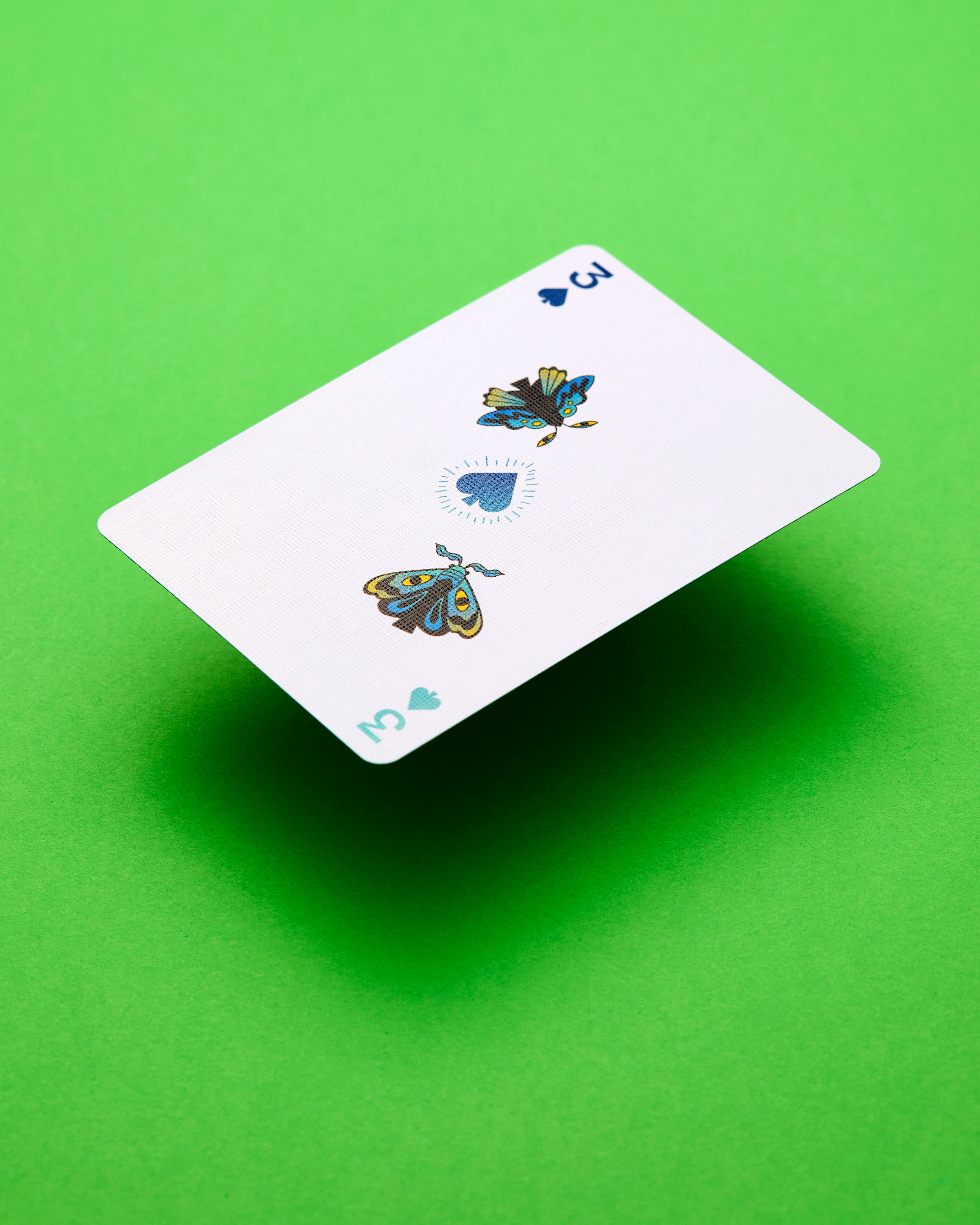 A single playing card, the three of spades, floating diagonally against a solid bright green background with a soft drop shadow.