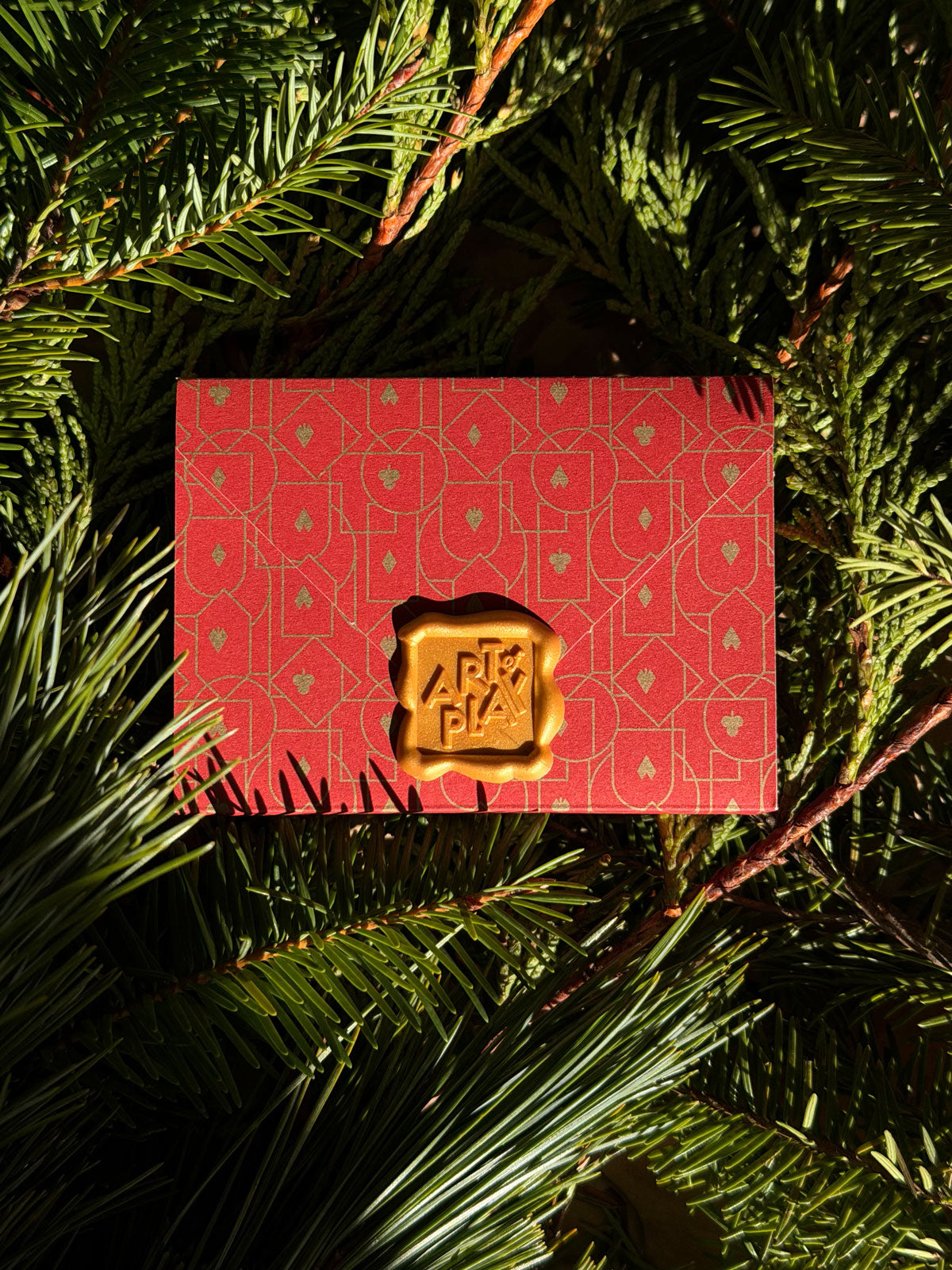 Mystery Deck of playing cards wrapped in red paper with gold stamp on green foliage.