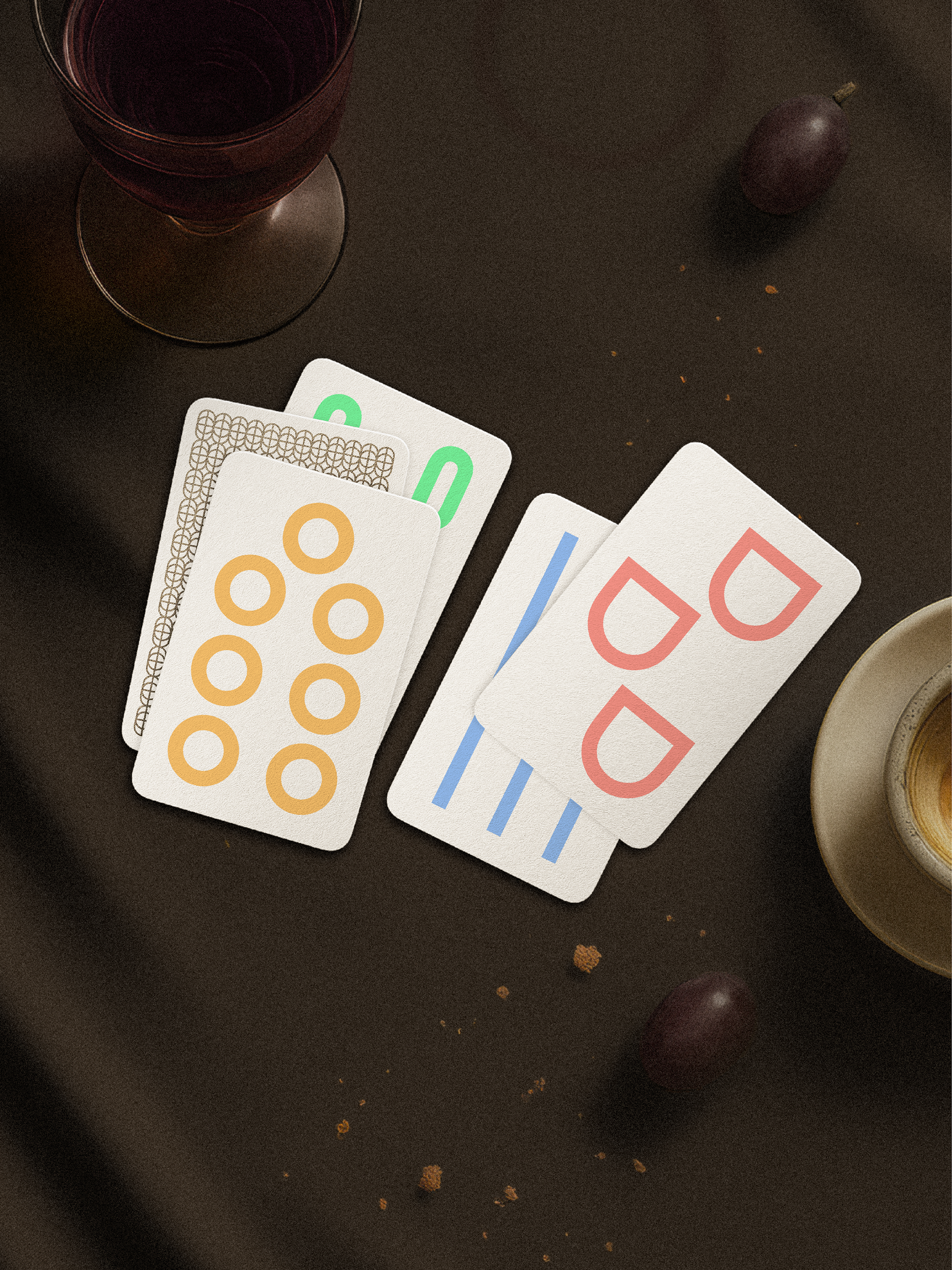 Four playing cards with unique symbols on a dark surface with a glass and fruit.