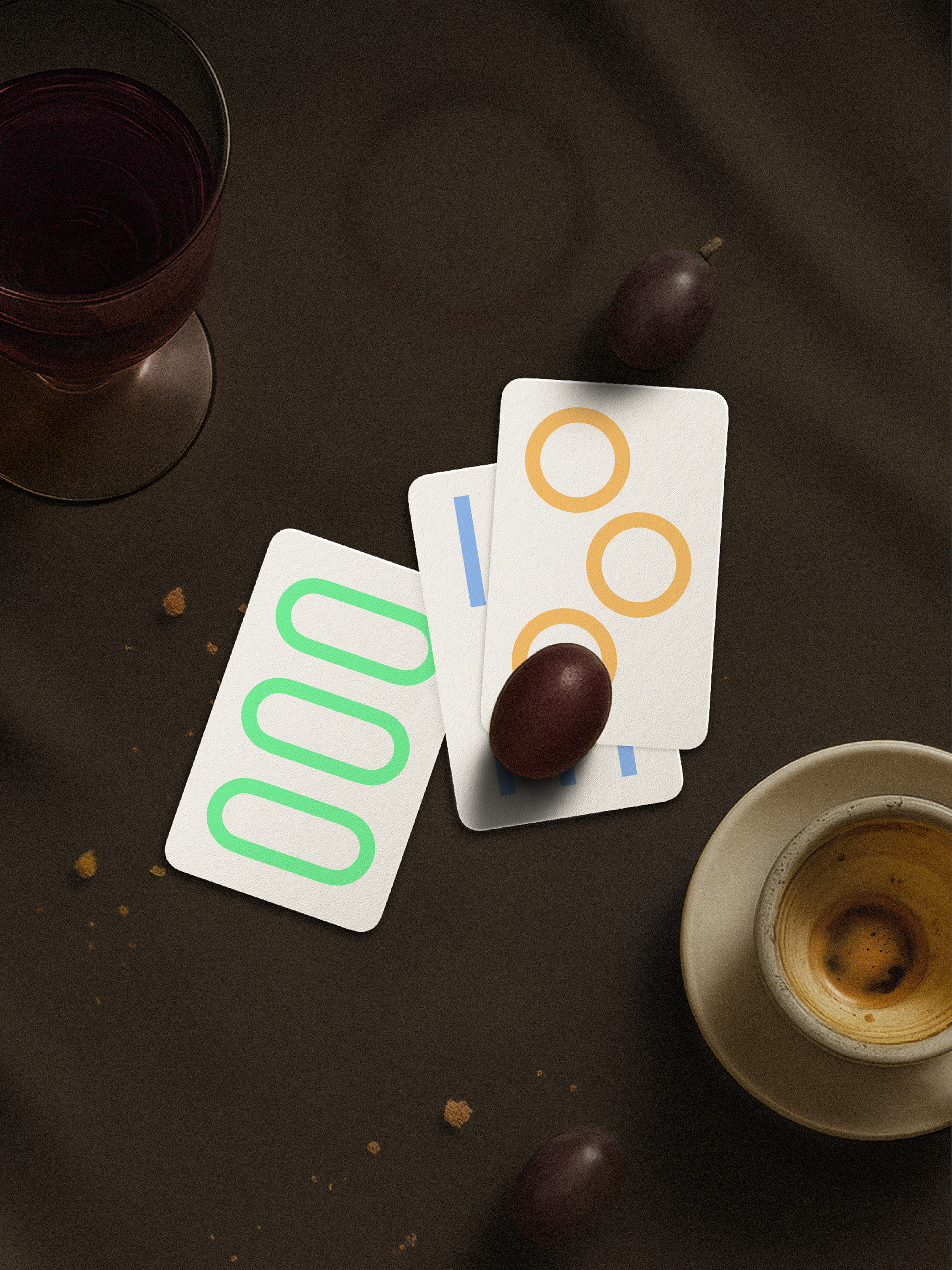 Three playing cards with colorful symbols on a dark surface with a glass and cup.