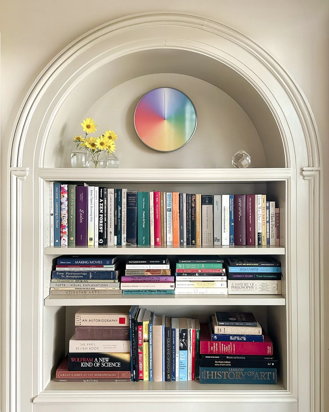 Bookshelf with books, a clock, and flowers in a decorative alcove.