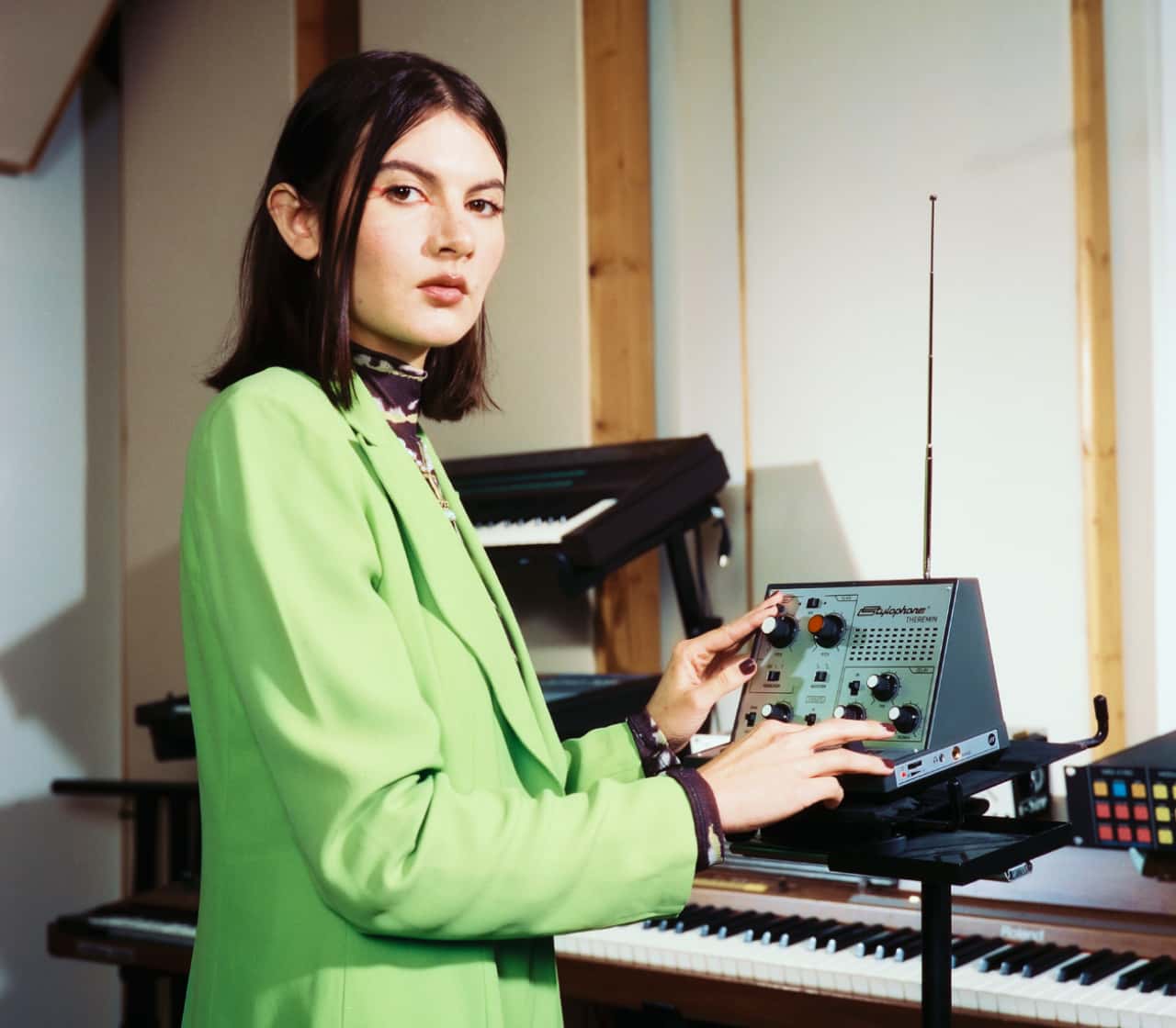 Person in a green jacket using electronic music equipment in a studio setting