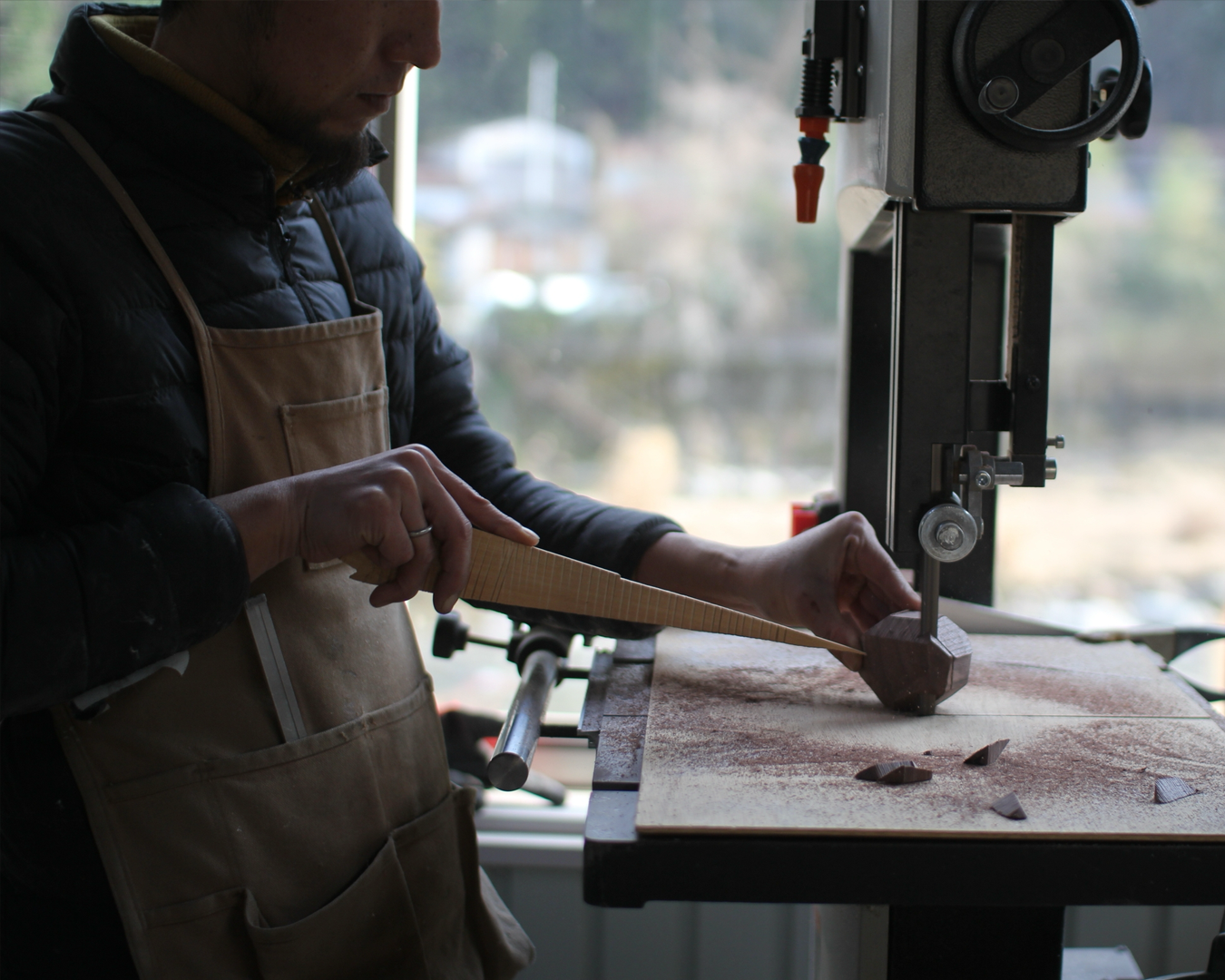 Person using a bandsaw in a workshop with a blurred outdoor background