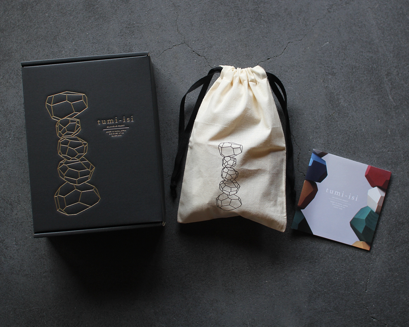 Product packaging with a black box, white drawstring bag, and colorful card on a dark surface.