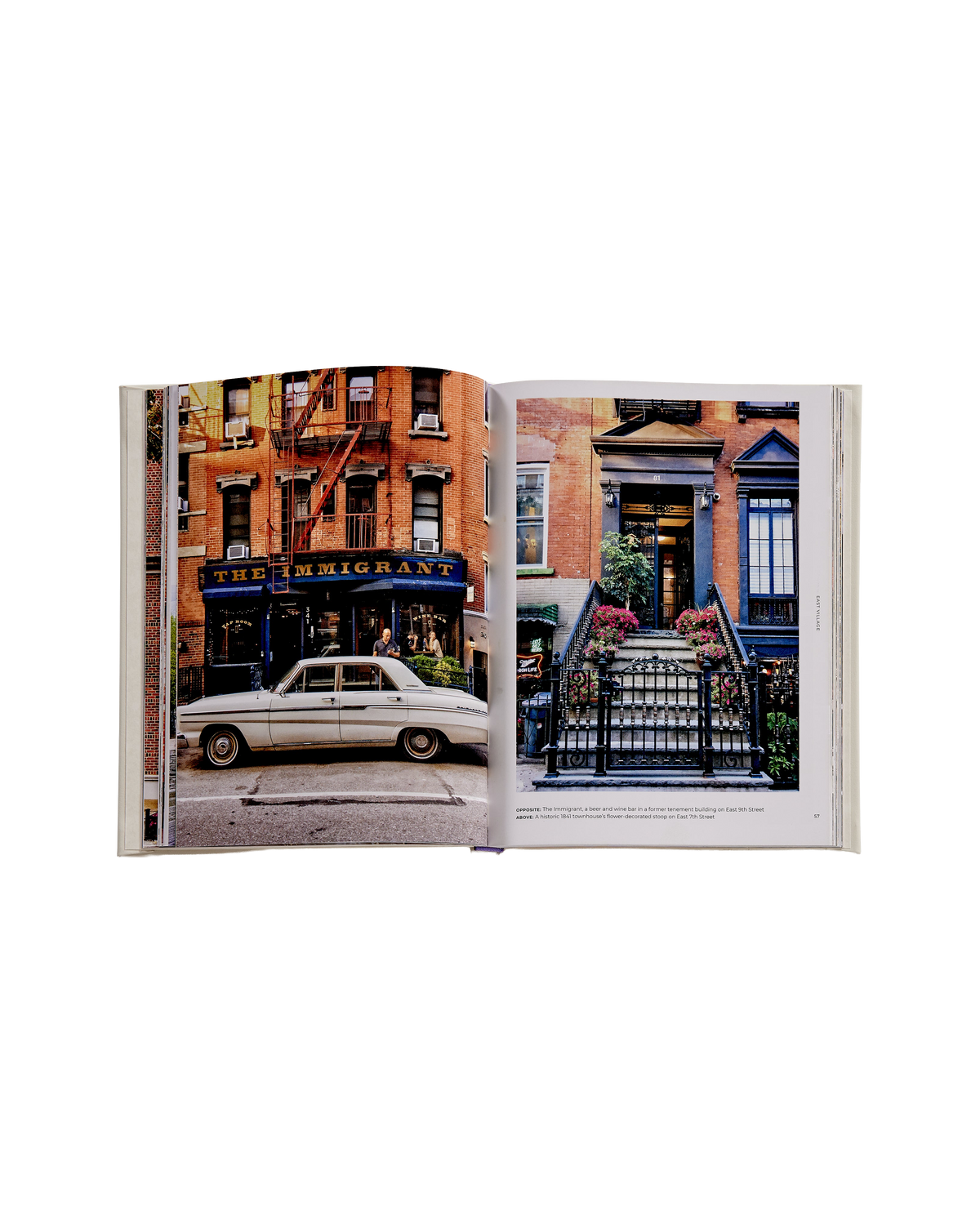 An open book displaying a two-page photographic print of an urban street scene with brick buildings, storefronts, a parked cream car, and a black wrought-iron staircase entrance.