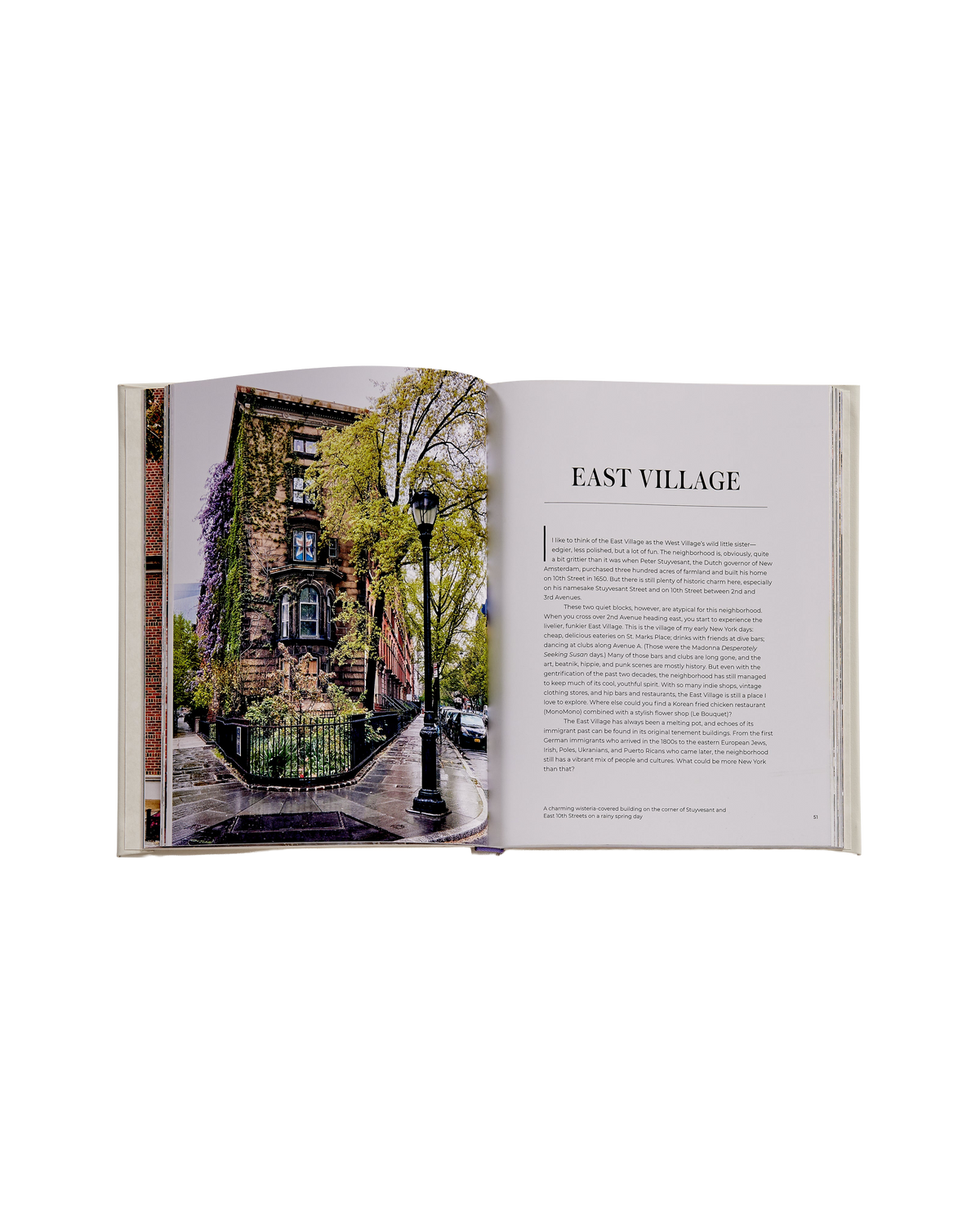 An open book showing a street photograph of an old brick apartment building on one page and an article titled 'EAST VILLAGE' with text on the next page, photographed on a white background.
